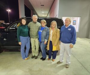 The United Way staff, board, and owner of the dealership are all taking a picture in front of a black Range Rover. They are giving the car away to a special someone.