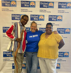 Three individuals are standing in front of a banner for the United Way, posing for a photograph. They are attending the Volunteer Luncheon.