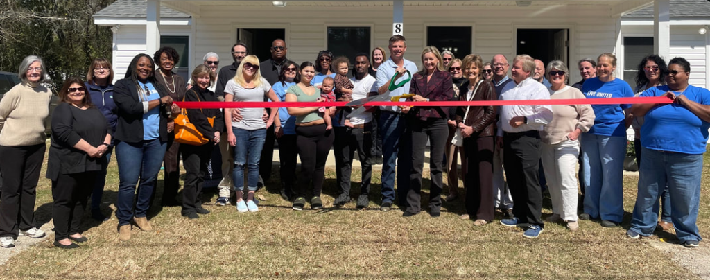 A ribbon-cutting ceremony took place at the United Way white building, and everyone involved gathered to take a picture in front of the building.