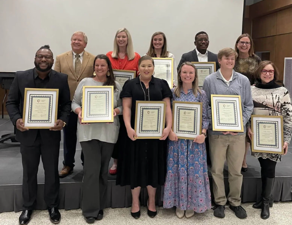 Imagine a group photo showing nine individuals from the Leadership Kershaw County Class of 2024. In the photo, all nine people are holding up the same award and are dressed up for the occasion.