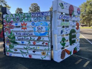 Two wooden planks painted white with a variety of fruits and vegetables crafted on them, along with vines that spell out "Camden Community Garden."