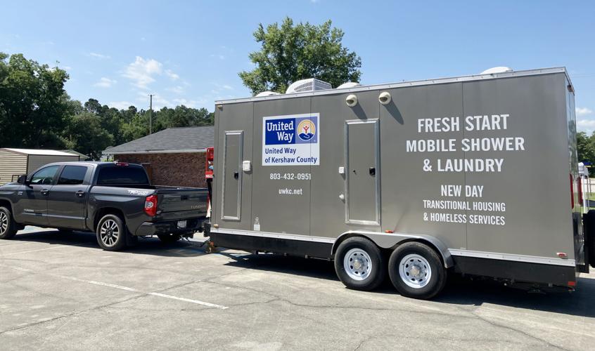 A truck is carrying a trailer that contains portable toilets and showers parked. There was a green sign indicating that the facilities were available for public use at no charge.