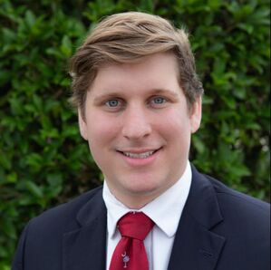 A young man was impeccably dressed in a blue suit that contrasted sharply with his pristine white shirt. His outfit was further accentuated by a bold red tie that added a splash of color to his ensemble.