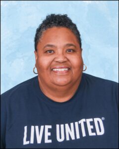 A person with dark skin wearing a dark blue shirt with the words "Live United" written on it. The person has short hair and is also wearing earrings.