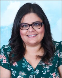 The person is wearing a colorful green shirt with pink, white, and purple flowers on it. Additionally, the person is wearing black glasses and has very dark black hair.