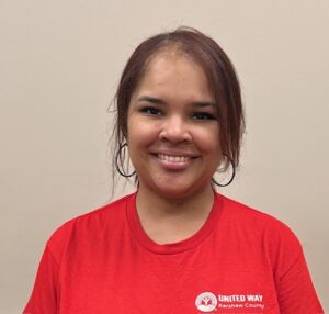 Woman in a red United Way Kershaw County shirt smiling in front of a plain beige background.