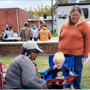 At a chili cookoff, a woman is reading a story to a child while the parents watch over them.