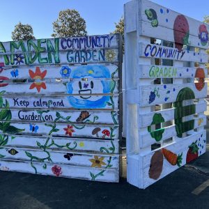 Two wooden planks painted white with a variety of fruits and vegetables crafted on them, along with vines that spell out "Camden Community Garden."