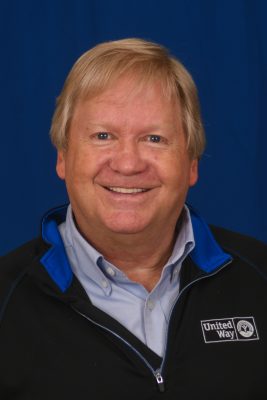 Donny Supplee is wearing a blue dress shirt with a black United Way pullover. Additionally, he has blonde hair.