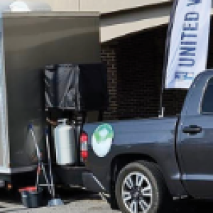 A truck is carrying a trailer that contains portable toilets and showers parked in front of a Food Lion in Camden, South Carolina. There was a green sign indicating that the facilities were available for public use at no charge.